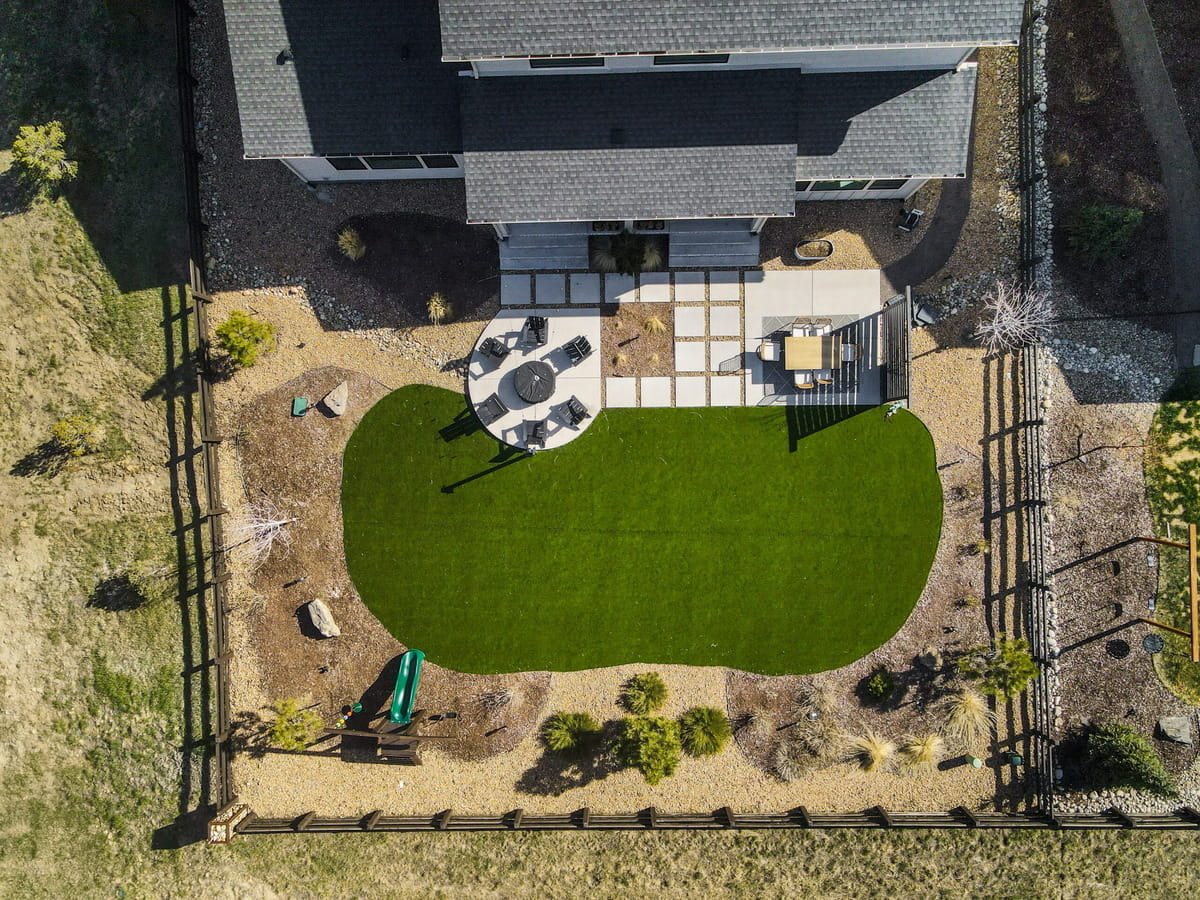 Aerial of a backyard with artificial turf, paver patio, seating and play area